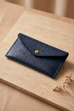 Cargar imagen en el visor de la galería, Cartera de cuero granulado azul oscuro apoyada sobre mesa de piedra con una única flor seca
