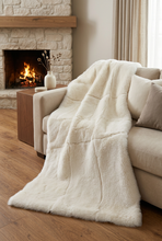 Cargar imagen en el visor de la galería, Manta clara sobre un sofá en un salón confortable con chimenea y decoración a juego, en formato vertical 2:3
