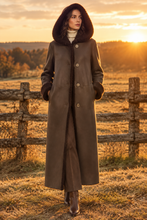 Cargar imagen en el visor de la galería, Modelo con el abrigo largo marrón con capucha de borreguito al atardecer junto a una valla de madera de campo
